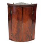 A 19thC figured mahogany bow fronted corner cabinet, with a chequer banded cornice, above two doors