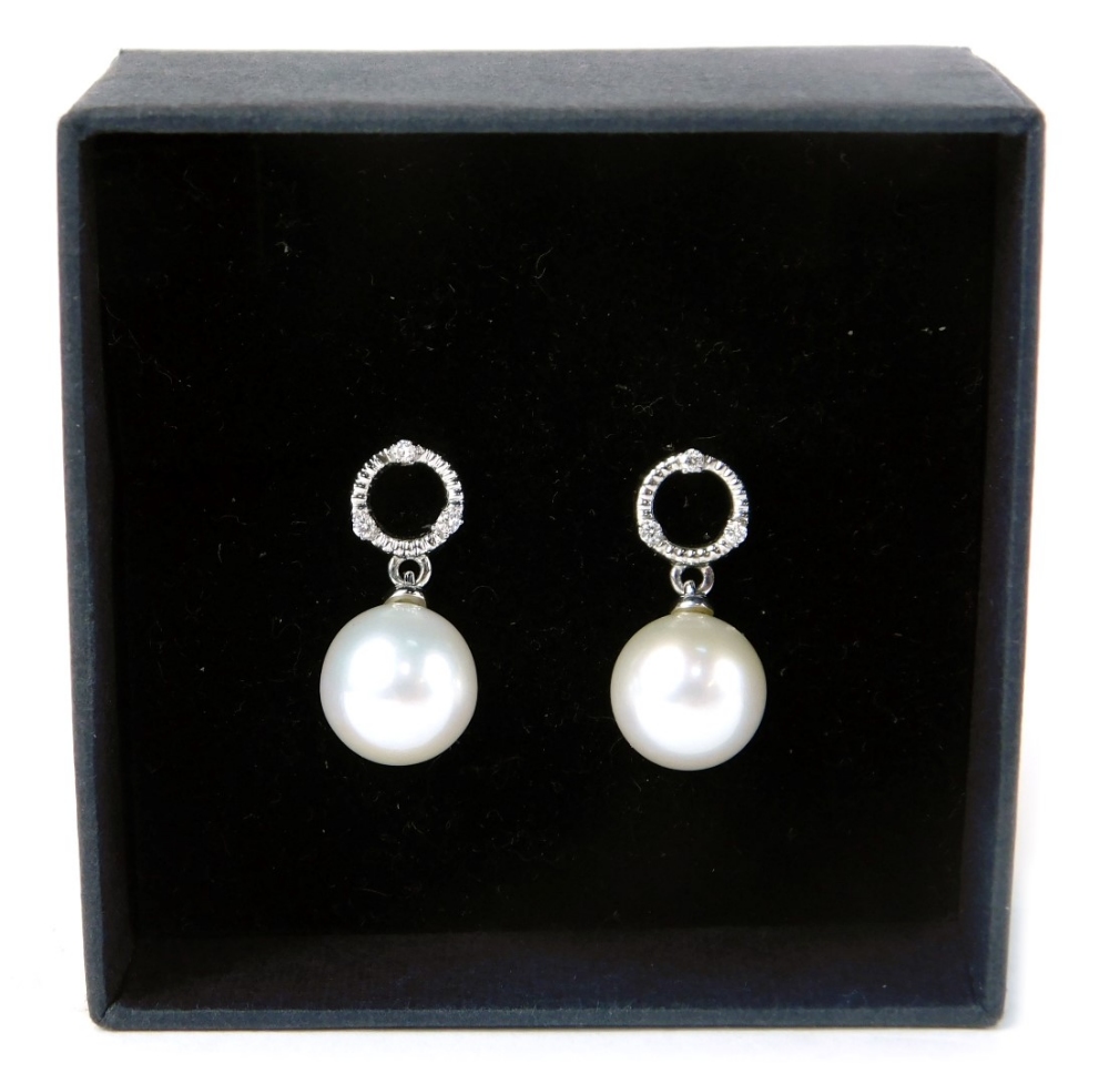 A pair of 9ct white gold pearl and diamond drop earrings, with a circle halo ring, set with three ti