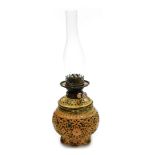 An early 20thC pottery oil lamp, with a clear glass chimney, the base with reticulated floral decora