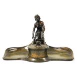 An early 20thC Art Nouveau bronze desk stand, the tray with figural surmount, behind an inkwell with