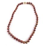 A string of cocoa cultured pearls, each bead 7mm wide, on a knotted string, with a 9ct gold bicolour