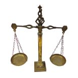 A pair of early 20thC brass balance scales, raised on an inverted Corinthian capitol column, above a