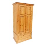 A pine wardrobe, with a moulded cornice above two panelled doors, the base with a drawer, on a plint