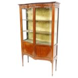 An Edwardian inlaid mahogany serpentine fronted display cabinet, with three shaped shelves and silk