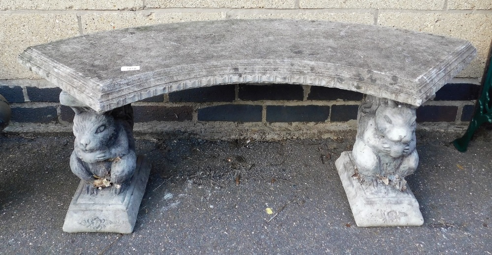 A concrete garden bench, the top of arched form raised on two squirrel cast plinths, 44cm high, 115c