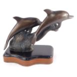 A bronze figure group of two dolphins, modelled riding the crest of a wave, raised on a serpentine m