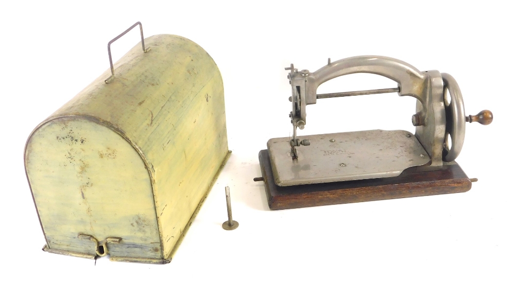 An early 20thC child's sewing machine, with chrome body in tin dome case on wooden base. 22cm high,