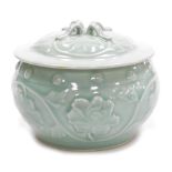 A Chinese celadon green circular jar and cover, decorated with trailing flower heads in relief, 15cm