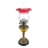 A brass oil lamp, with a cranberry frosted glass shade, and chimney, on brass embossed body, on an e