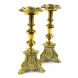 A pair of early 20thC brass pricket altar candlesticks, each on a tripod base, embossed with the hea