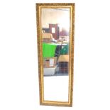 A rectangular gilt framed wall mirror, decorated with foliate scrolls, 113cm x 37.5cm.