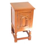 An oak bedside cupboard, with an arched carved panelled door opening to reveal a single shelf, raise