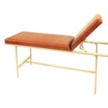A 20thC metal framed medical examination couch, upholstered in red leatherette, with an adjustable h