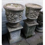 A pair of reconstituted stone garden planters, each with a circular planter with floral design, on a