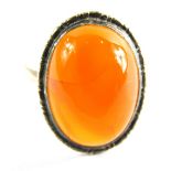 An orange agate dress ring, with cabochon stone in white metal band, unmarked, ring size M½, 3.7g al