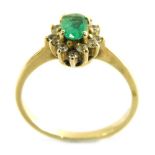 An emerald and diamond cluster ring, with pale green oval emerald in claw setting surrounded by twel