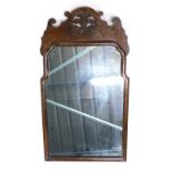 A 20thC walnut framed mirror, with shaped glass, surmounted by a pierced floral emblem, 64cm x 37cm.