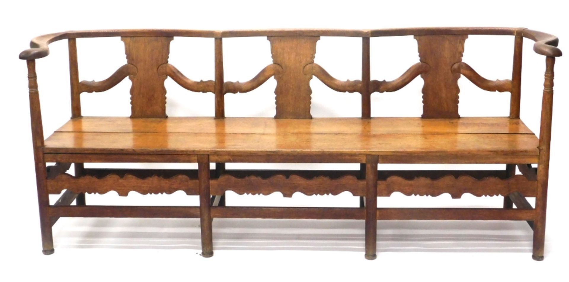 An oak Arts and Crafts style settle, with serpentine back, on turned supports with a carved frieze,