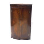 A mahogany hanging corner cabinet, with a carved top raised above two flame mahogany doors, with she