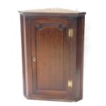 A late 18thC oak hanging corner cabinet, the panelled door revealing a fitted interior, with two she
