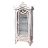 A French style painted cabinet, the arched glass door revealing three shelves surmounted by a scroll