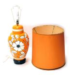 An orange retro pottery table lamp, with fixed top, vibrantly decorated with flowers, on a white an