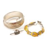 A silver bangle, floral and foliate engraved, on a snap clasp, with safety chain as fitted, Siam sil