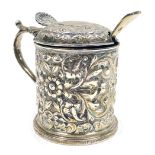 A Victorian silver mustard pot, the body and lid embossed with flowers, leaves and scrolls with a sh