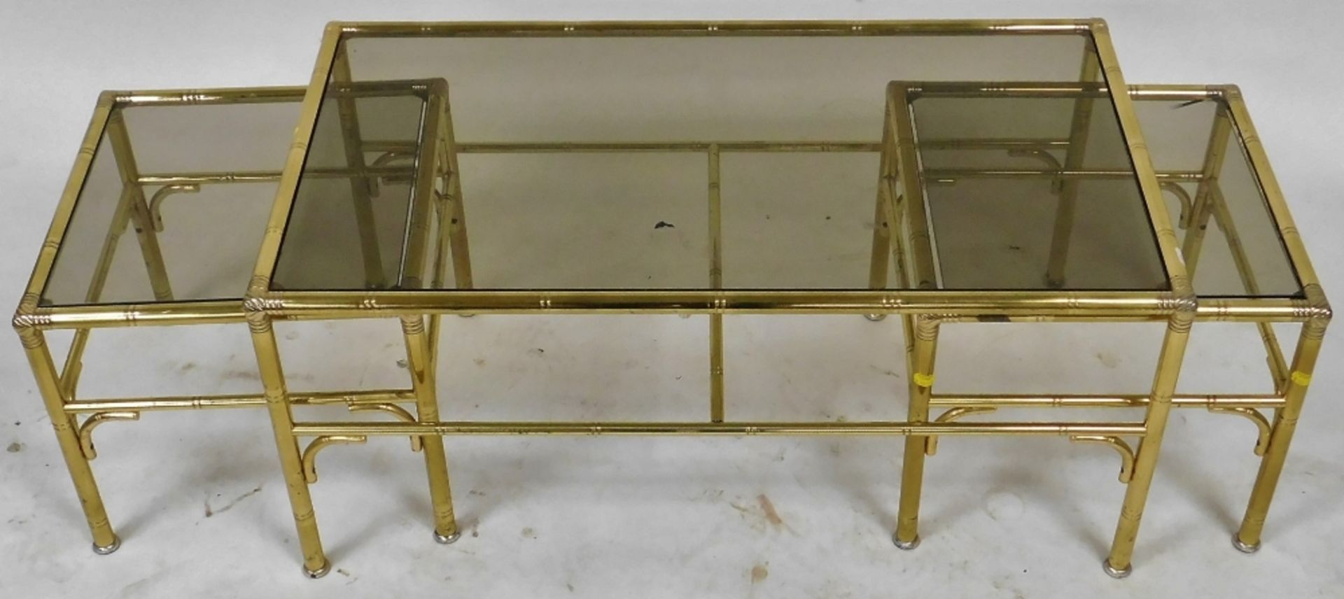 A late 20thC brass nest of occasional tables, inset with smoky glass, comprising a rectangular table