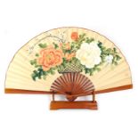 A modern Oriental painted fan, depicting peonies and blossom, on a fan stand.