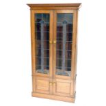 An early 20thC oak Arts and Crafts bookcase, the moulded cornice raised above a pair of lead glass p