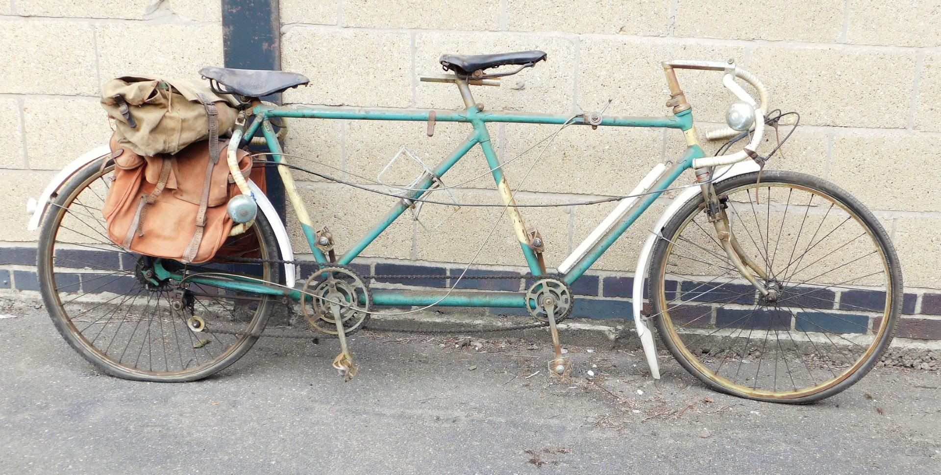A vintage Reynolds tandem bicycle, in green trim, with leather seats and various canvas saddlebags.