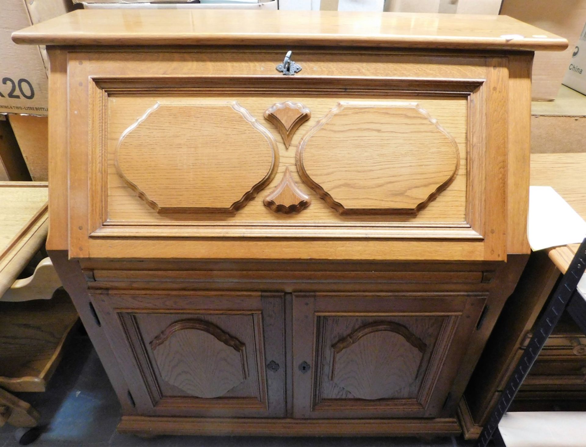 An oak bureau, the carved fall enclosing a fitted interior, the base with two panelled cabinets, 120