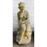 A reconstituted stone garden figure, of a semi clad female, perched on a rock, 61cm high.