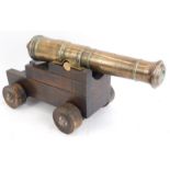A 19thC brass table cannon, numbered 5, on a stepped wooden base, 23cm high, 31cm wide.