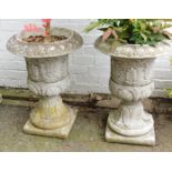 A pair of reconstituted stone garden urns, of semi fluted form, decorated with acanthus leaves, on s