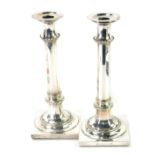 A pair of Edwardian plated candlesticks, each with a tapered and beaded stem, on a square set base,