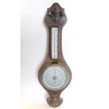 A 20thC oak cased two dial barometer and thermometer, the heavily carved case with 12cm diameter bar