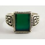 A signet ring, set with square cut jade in a rubover setting, on a white metal band with Greek key b