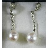 A pair of 18ct white gold diamond and pearl drop earrings, the waved stud with chain link, with a cu