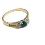 An 18ct gold emerald and diamond dress ring, claw set with green stone flanked by two small white st