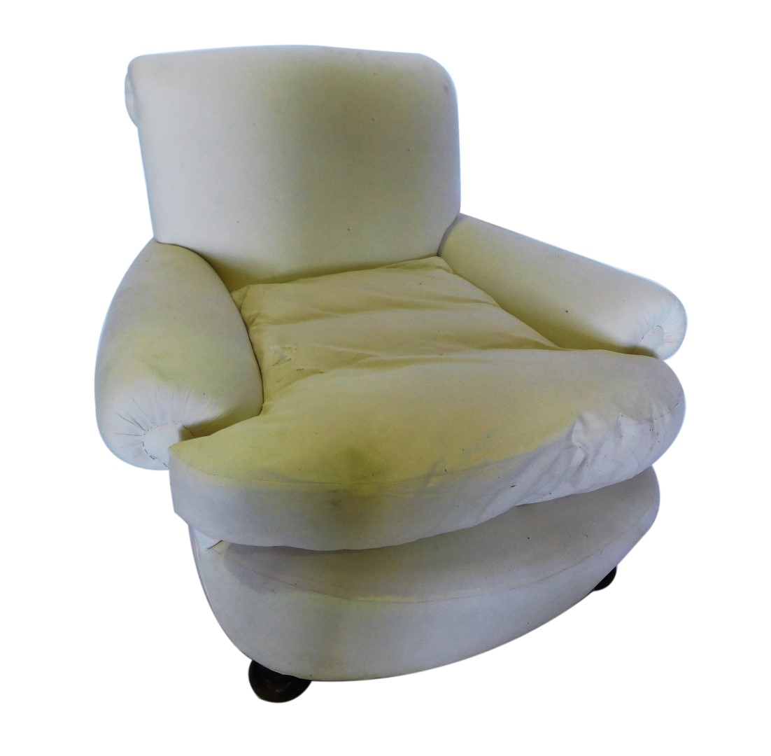 A broad deep seated early 20thC armchair, upholstered in white calico, on bun feet.
