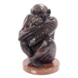 An early 20thC French bronze figure of a monkey, modelled seated with arms clasped, raised on a red