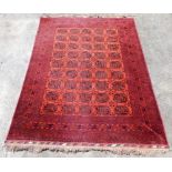 A Baluch red ground rug, decorated with fourty-five central medallions, within repeating floral bord