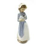 A Nao porcelain figure of a girl, modelled standing wearing a mobcap, with a puppy in her arms and d