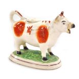 A late 19thC pottery cow creamer, with red markings, raised on an oval base, 17cm wide. (AF)