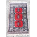 A Bokhara red ground prayer rug, with three central motifs, within repeating geometric borders, 98cm