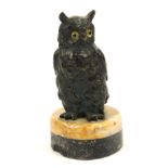 An early 20thC bronze owl ornament, with yellow glass eyes, on a two tone marble circular base, 12cm