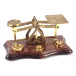 An early 20thC brass postage scales, on a shaped base, with five weights, 17cm wide.