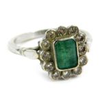 An 18ct white gold emerald and diamond cluster ring, with a central rectangular cut emerald in rub o
